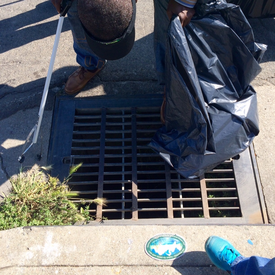 A volunteer with a trash bag and grabber inspects a stormwater drain